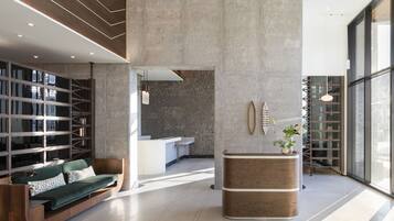 A modern lobby with a wooden reception desk, a green sofa, and a large window offering a view of the outside.