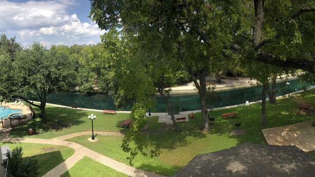 A swimming pool surrounded by trees and benches, with a clear view of the water. - Beautiful Updated Condo With Direct River View From Balcony!  We Love Dogs! (New Braunfels)