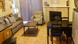 A living room with a sofa, armchair, coffee table, dining table, chairs, fireplace, and decorative wall art. - Beautiful Updated Condo With Direct River View From Balcony!  We Love Dogs! (New Braunfels)