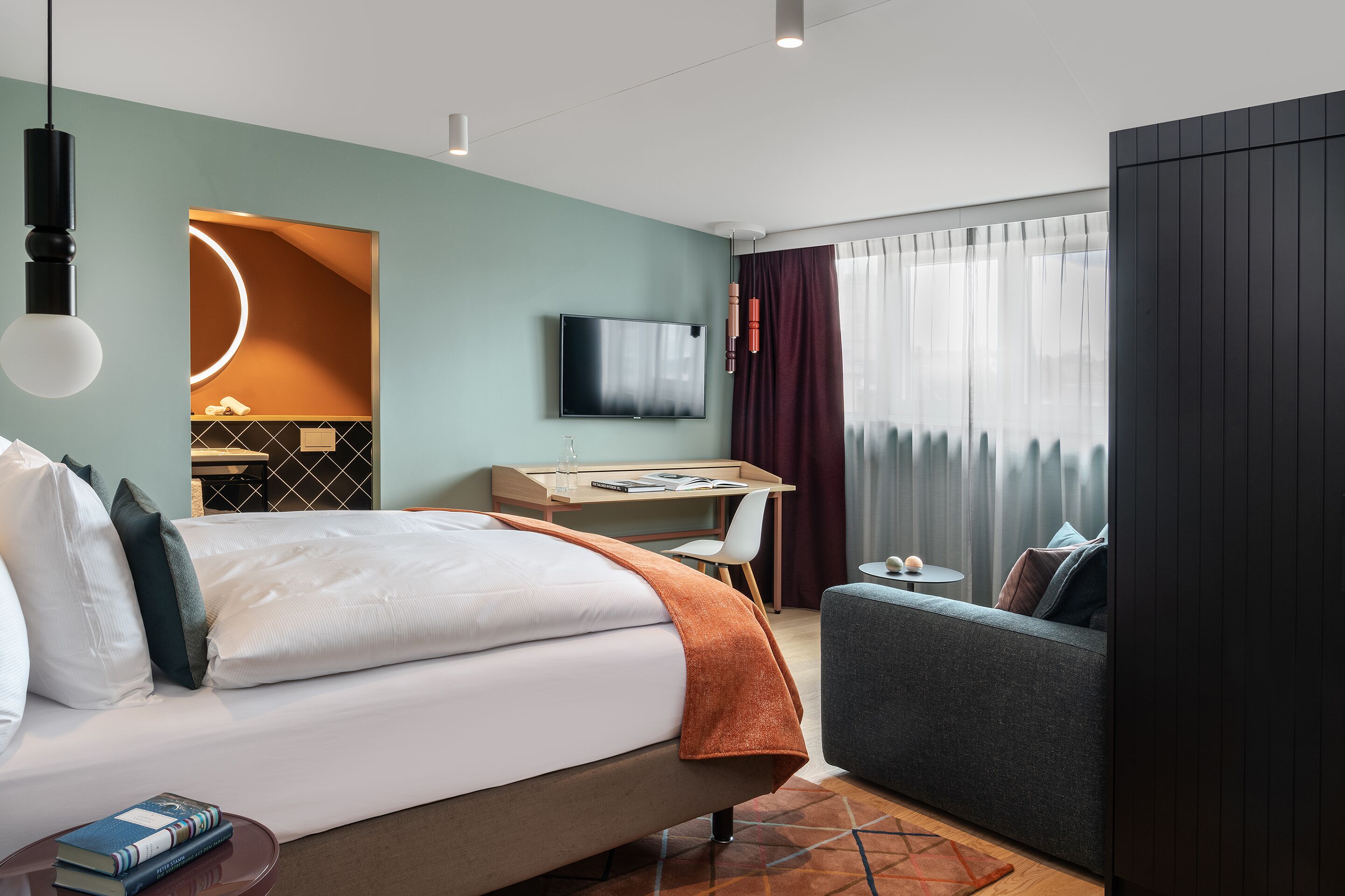 A modern hotel room with a bed, a desk, a TV, and a sofa.