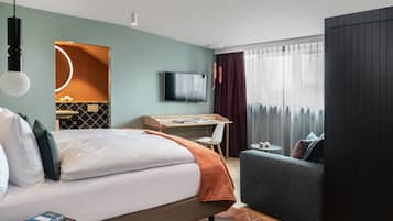 A modern hotel room with a bed, a desk, a TV, and a sofa.