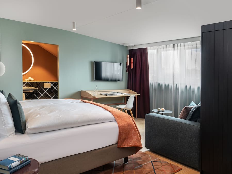 A modern hotel room with a bed, a desk, a TV, and a sofa.