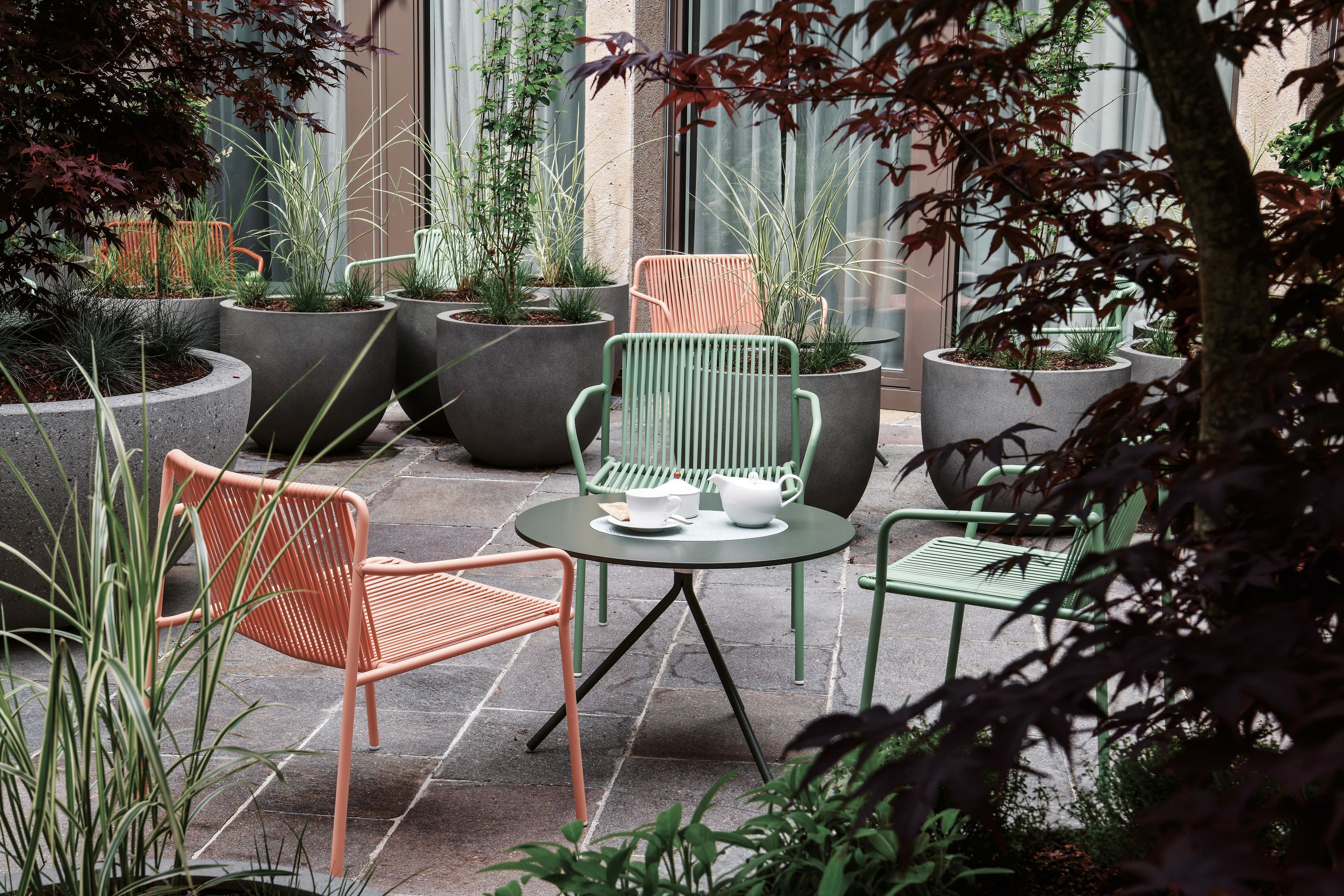 Eine Terrasse mit mehreren Stühlen und Tischen, umgeben von gro ßen Pflanzgefäßen mit verschiedenen Pflanzen.