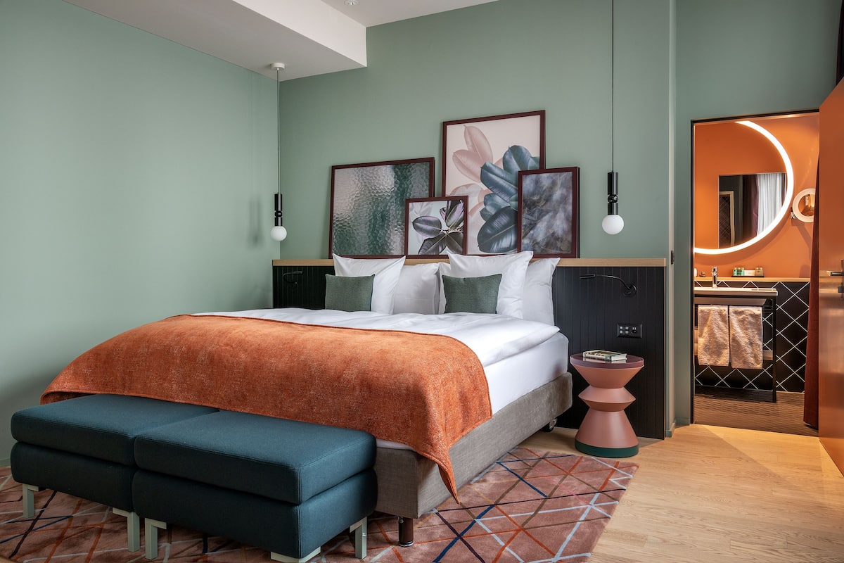 Ein modernes Schlafzimmer mit Bett, Nachttischen, einer Bank und Kunstwerken an der Wand.