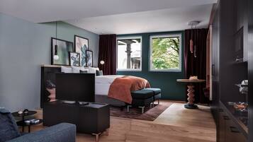 Ein modernes Schlafzimmer mit Bett, Schreibtisch, Stuhl, Sofa und Fenster mit Blick auf Grünflächen.
