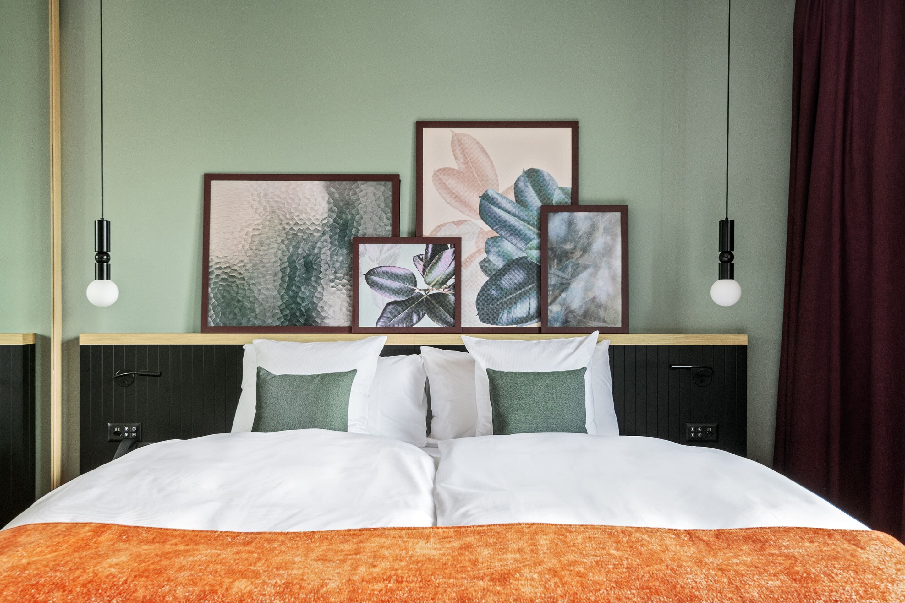 A neatly made bed with white and orange bedding, a headboard with framed artwork, and two bedside tables with black lamps.