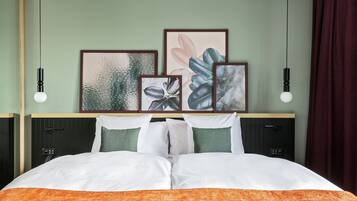 A neatly made bed with white and orange bedding, a headboard with framed artwork, and two bedside tables with black lamps.