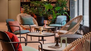 A modern lounge area with wicker chairs, a coffee table, and a bookshelf filled with books and decorative items. - Sorell Boutique-Hotel St. Peter Zürich (Zürich)