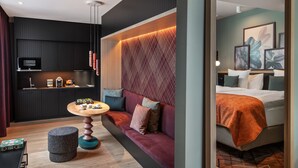 A modern hotel room with a sofa, a small round table, a TV, and a bed with an orange blanket. - Sorell Boutique-Hotel St. Peter Zürich (Zürich)