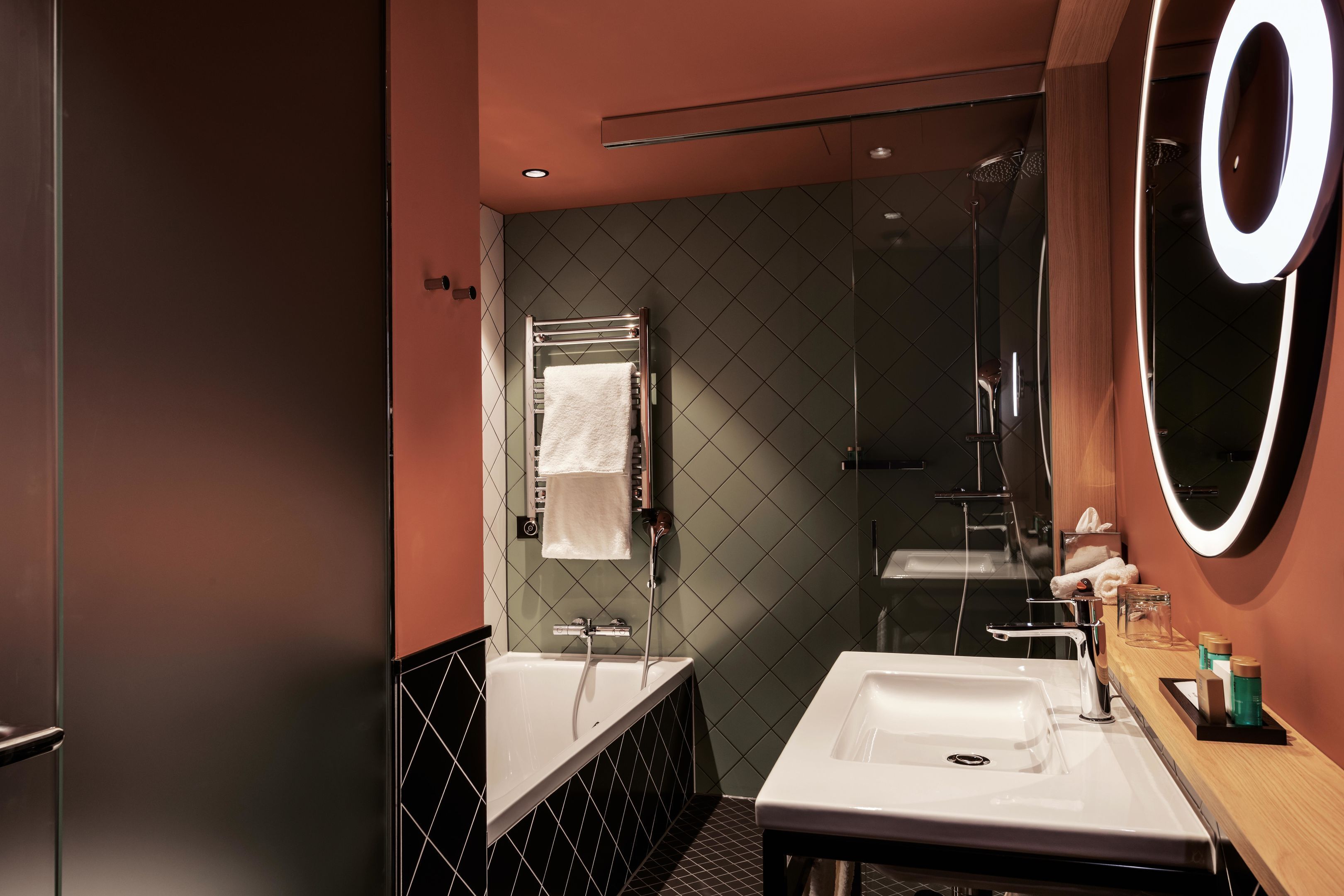 A modern bathroom with a glass shower enclosure, a white sink, and a large mirror with a circular light.