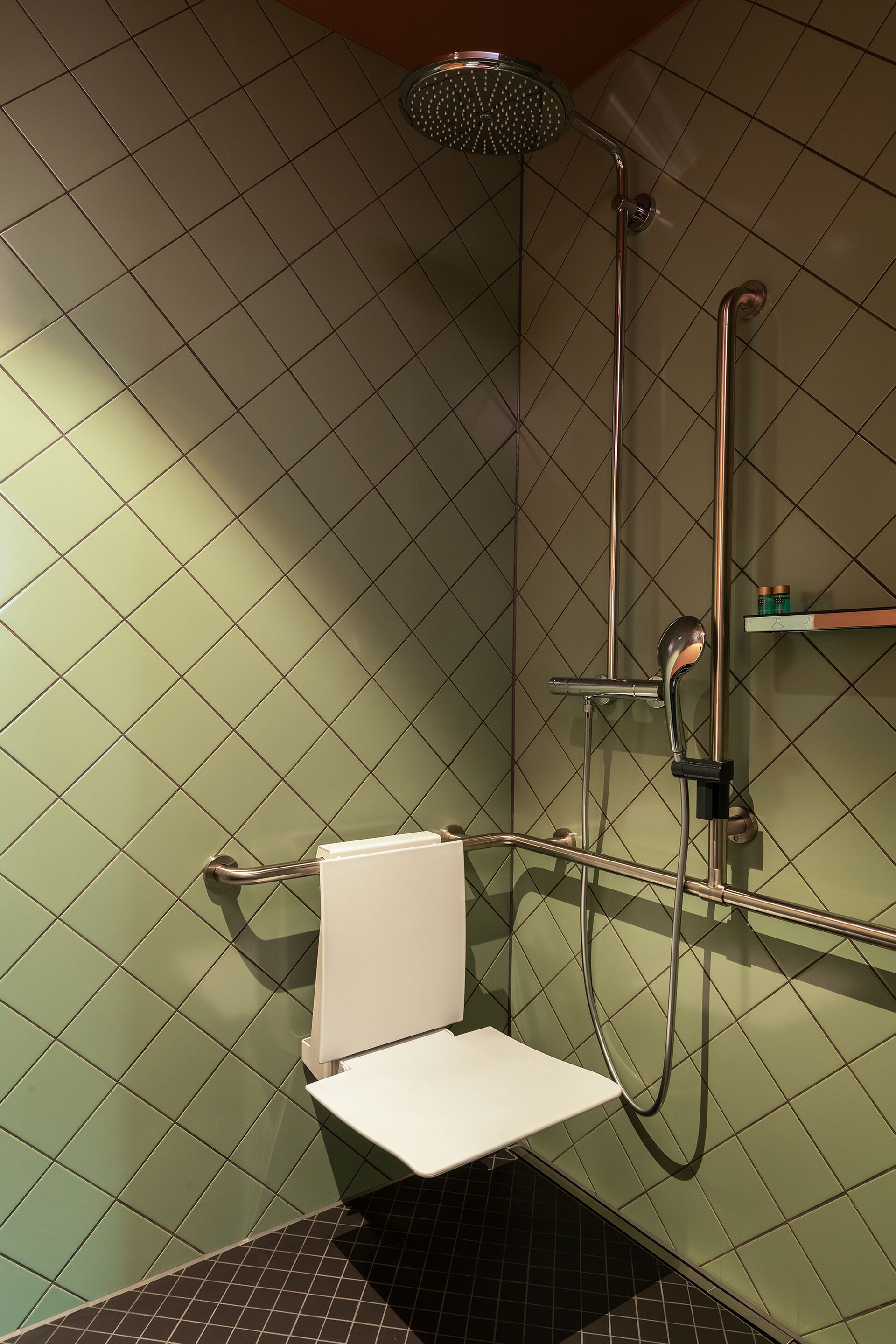 Eine Dusche mit Duschbrause, Wandarmatur und kleinem Ablagefach für Toilettenartikel.