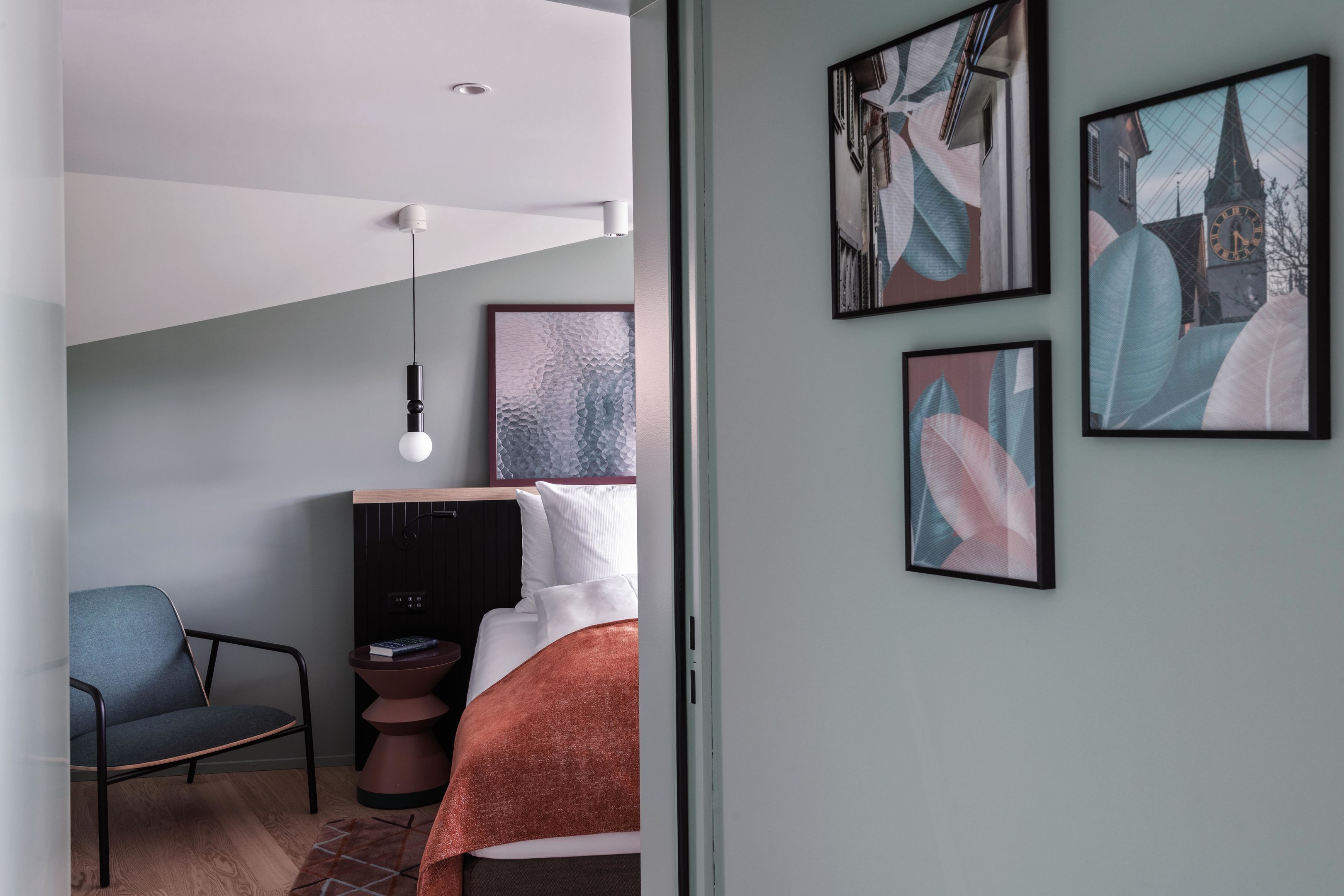 Ein modernes Schlafzimmer mit Bett, Sessel, Nachttisch und Wandbildern.
