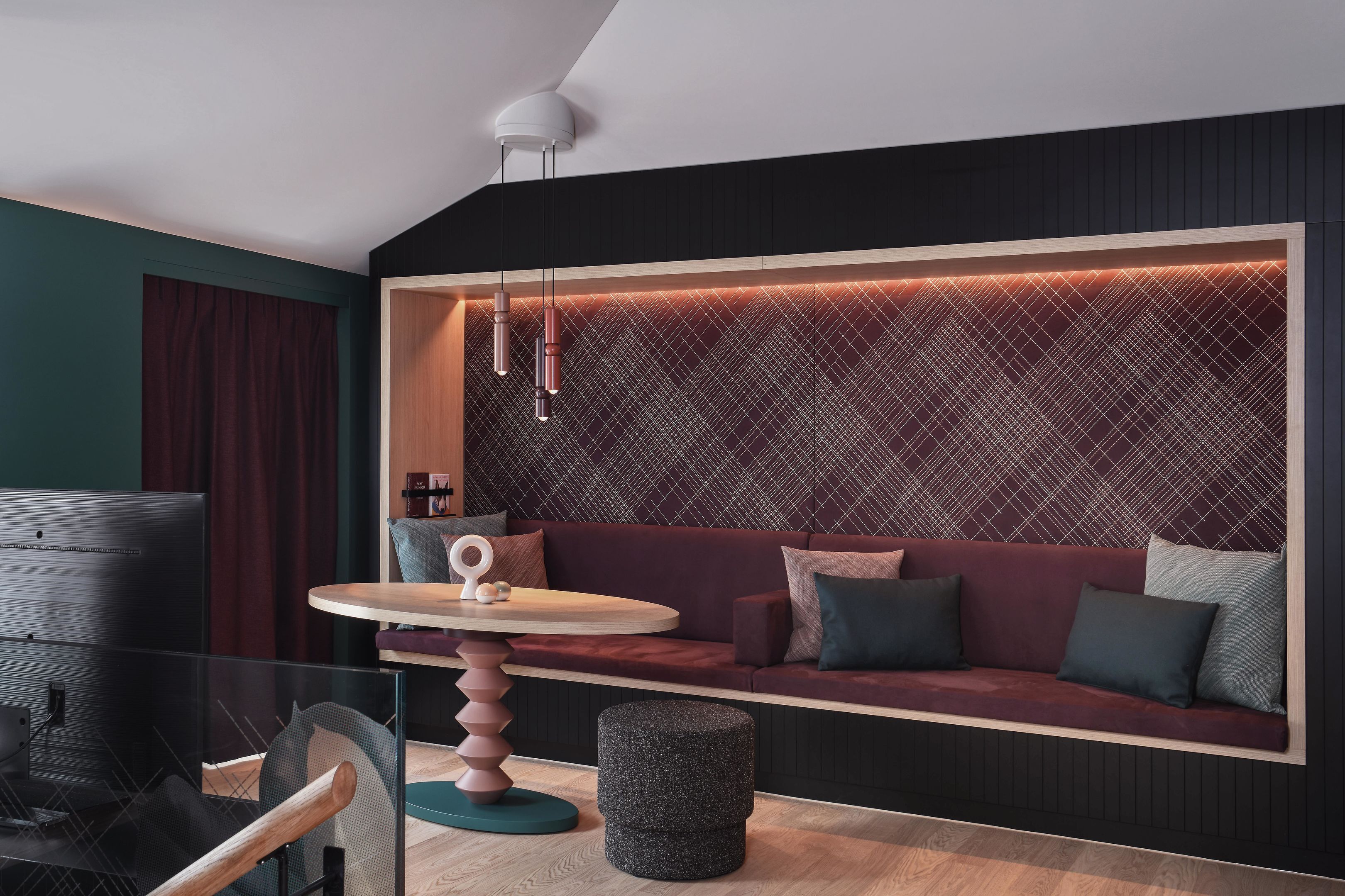 Una habitación moderna con una pared de acento verde oscuro, un sofá rojo con cojines, una mesa redonda con un objeto blanco y un papel tapiz estampado detrás del sofá.
