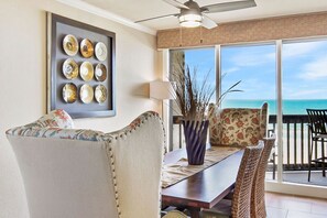 A room with a large window overlooking the ocean, a ceiling fan, and a dining area with wicker chairs and a table. - Sandpiper Condominiums 603L, Panoramic Gulf Views w/ direct access to Mustang Island/Port A beaches. (Port Aransas)