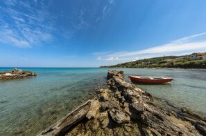 A rocky shoreline with clear water and a red boat tied to a post. - Villa Eleni-2nd Floor Maisonette with Ocean panorama terrace (Alikanas)
