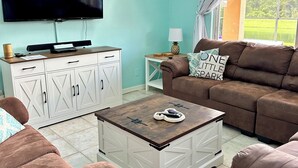A living room with a television, white cabinets, a brown sofa, and a coffee table. - 8BR lakefront Disney home w themed rms HarryPotter Frozen ToyStory Mario Royal (Kissimmee)
