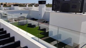 Une terrasse sur le toit dotée d’une balustrade en verre, un petit coin salon avec des coussins et une vue sur le paysage urbain.