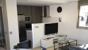 Un appartement moderne comprenant une cuisine, un coin repas et un salon. Il est équipé d’une télévision, d’une petite table et d’un canapé.