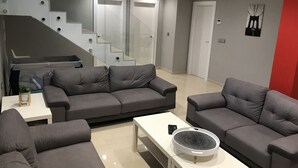 Un salon moderne avec des canapés gris, une table basse blanche et un escalier doté de rampes en verre.