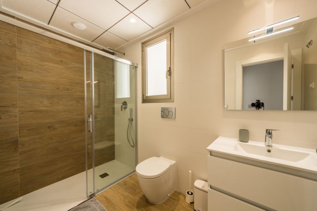 Een moderne badkamer met een douchecabine van glas, een toilet, een wastafel en een spiegel.
