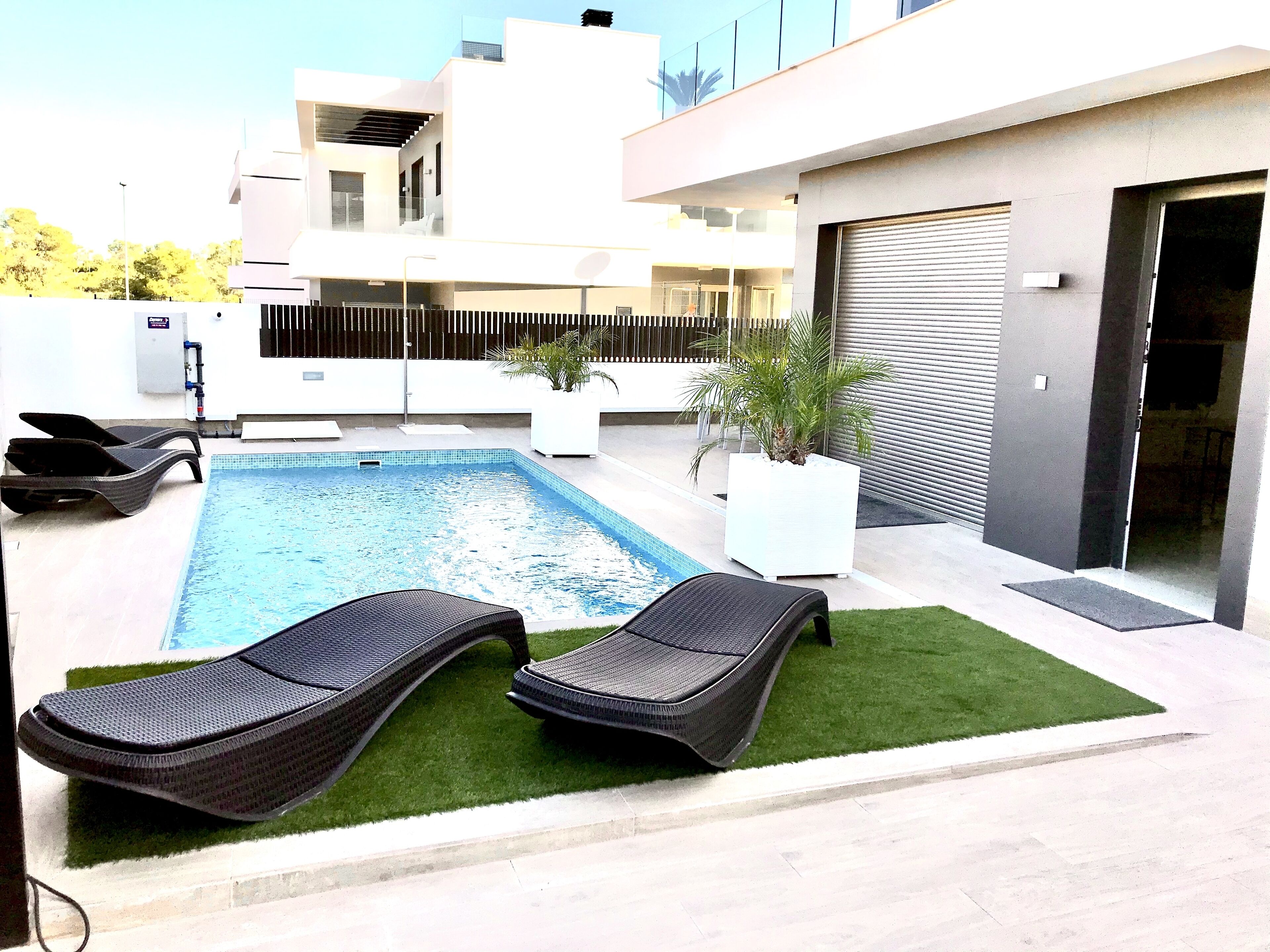 Un espace piscine extérieur moderne, comprenant deux chaises longues, une petite piscine et une plante en pot.