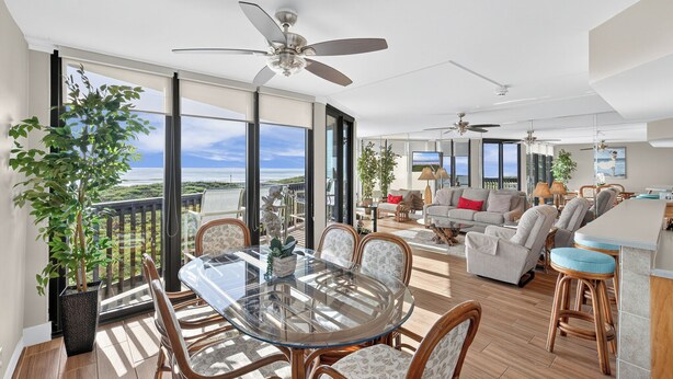 Un vaste espace de vie avec balcon, de grandes fenêtres et une table à manger avec des chaises.