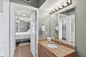 Une salle de bain moderne avec un comptoir en granit, un lavabo, un miroir et un ventilateur de plafond.