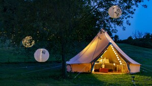 Een tent met een bed en een tafel, omringd door bomen en verlicht met lichtslingers.