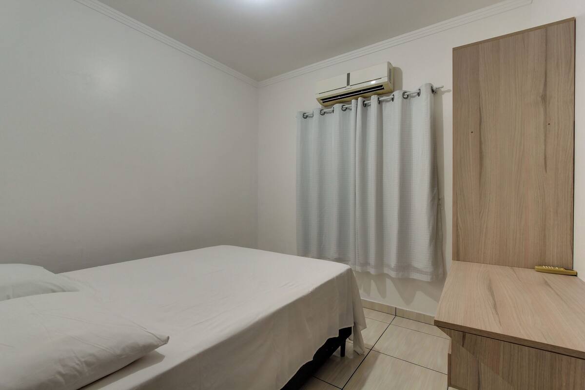 A bedroom with a bed, a wooden nightstand, a mirror, and an air conditioning unit.
