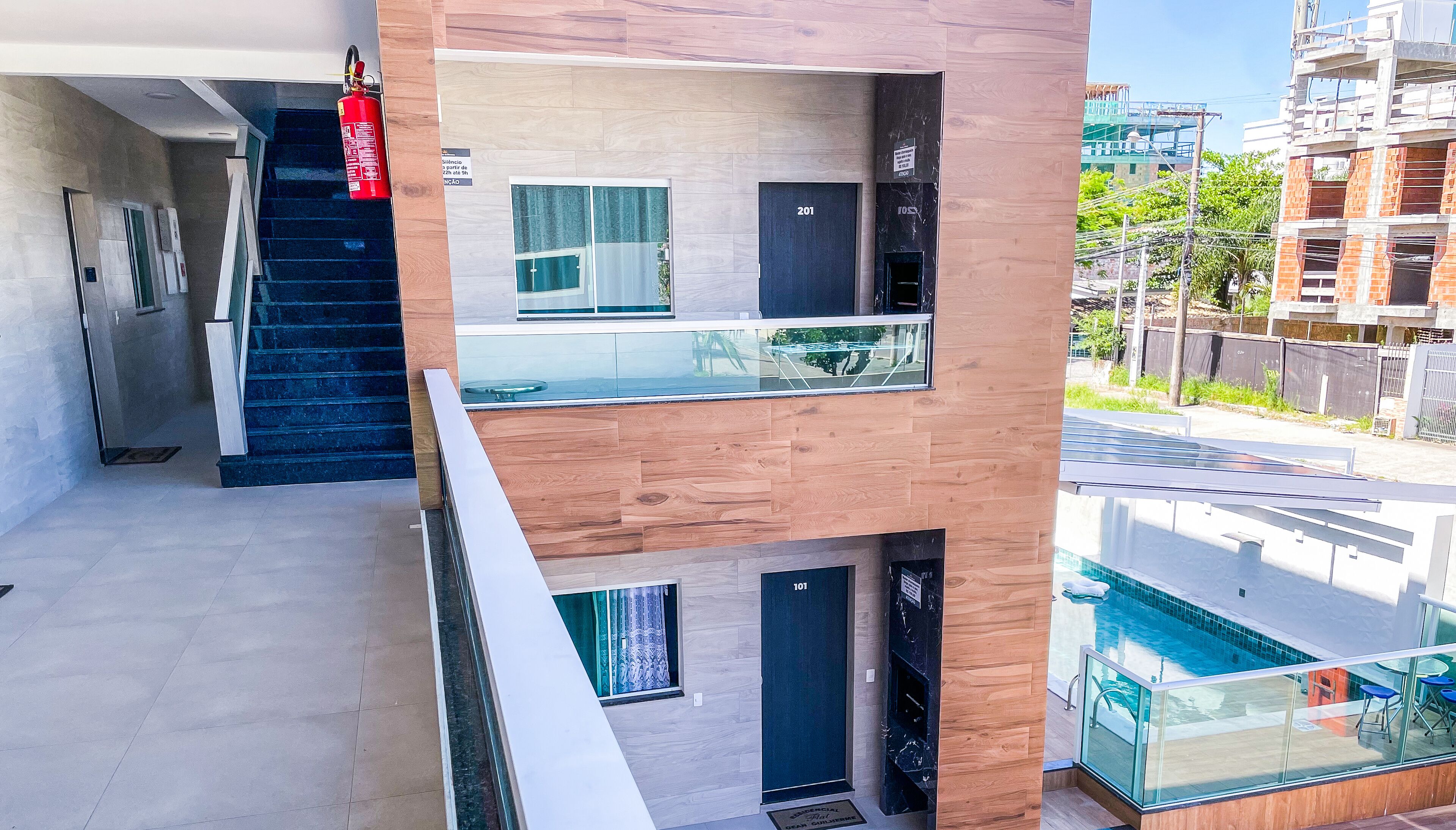 A modern building with a glass balcony, a fire extinguisher, and a view of a swimming pool.