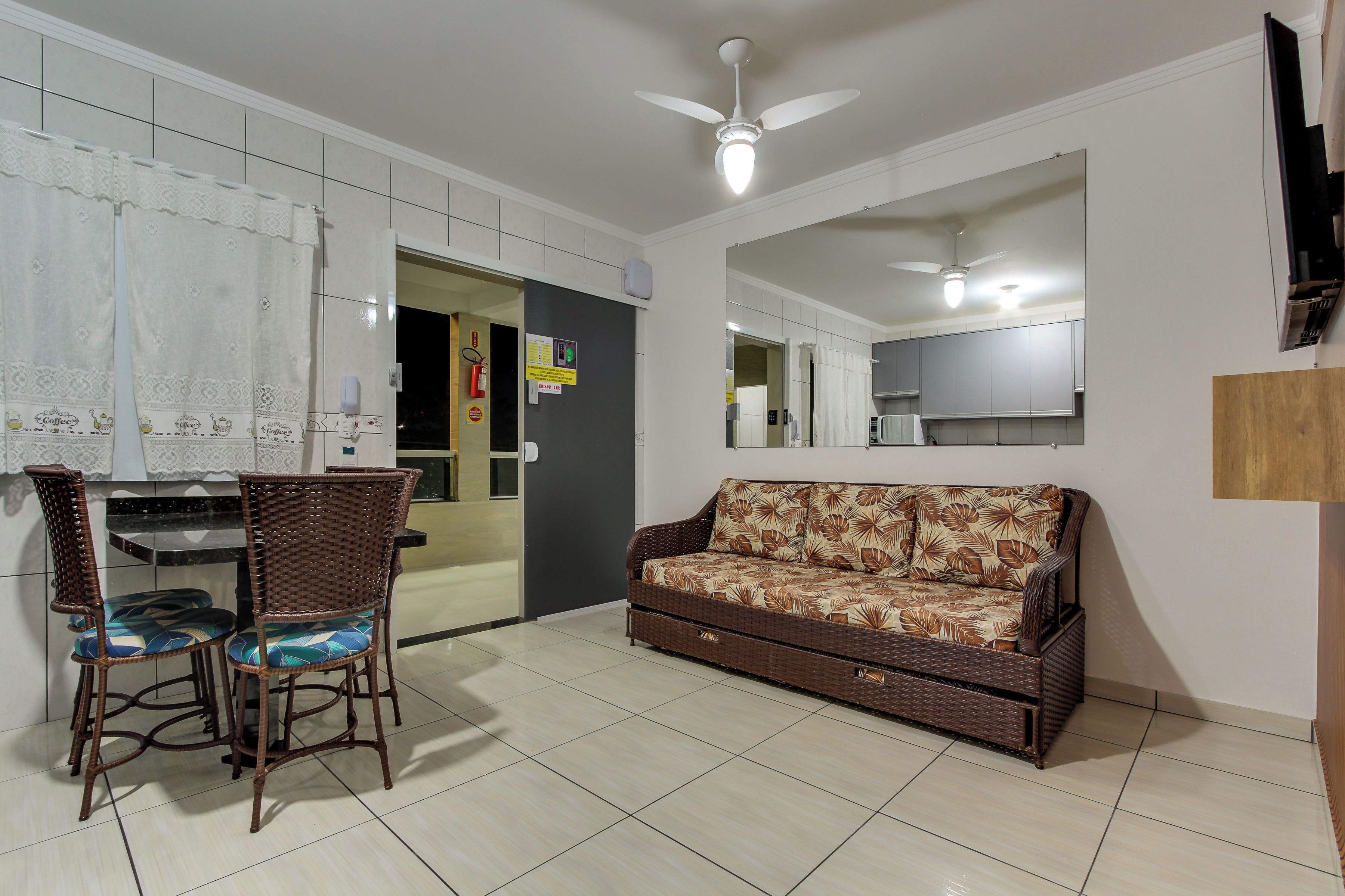 A living room with a sofa, two wicker chairs, a dining table, and a ceiling fan.