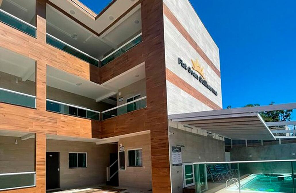 A modern hotel with a two-story structure, a covered outdoor pool, and a prominent logo on the facade.