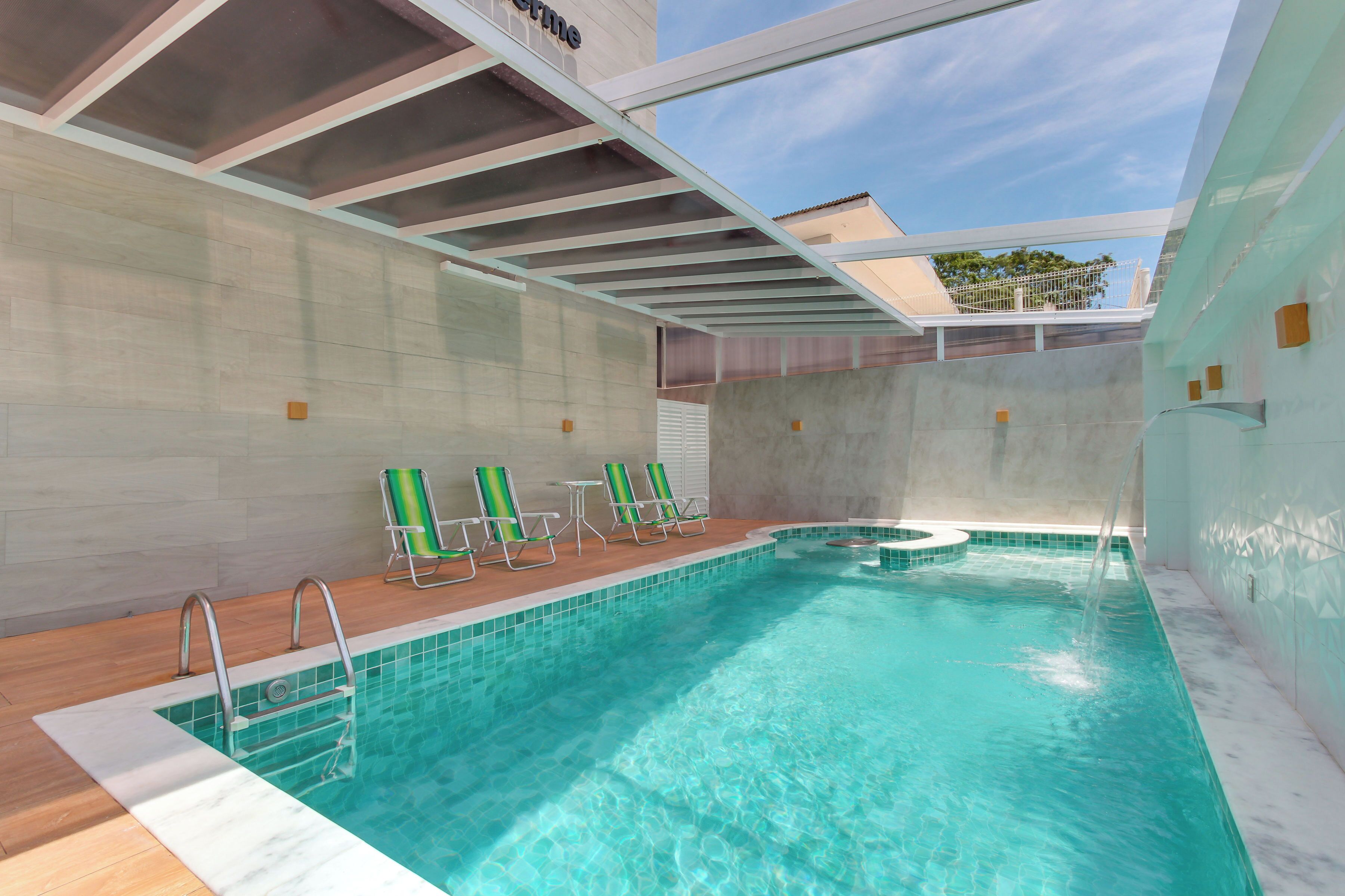 An indoor swimming pool with clear blue water, a wooden deck, and green lounge chairs.