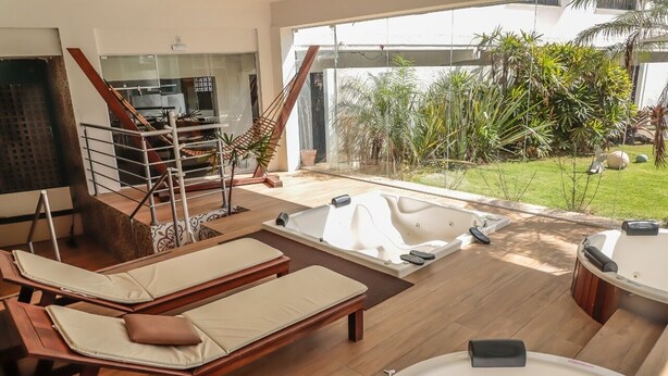 A modern spa area with two sun loungers, a large bathtub, and a staircase leading to a glass door. - Scaini Palace Hotel (Balneario Arroio do Silva)
