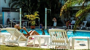 A pool area with white lounge chairs, a potted plant, and a tiled pool. - Scaini Palace Hotel (Balneario Arroio do Silva)