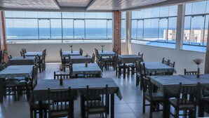 A restaurant with multiple tables and chairs, large windows offering a view of the ocean. - Scaini Palace Hotel (Balneario Arroio do Silva)