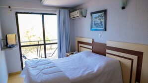 A hotel room with a bed, a desk, an air conditioning unit, a window with curtains, and a framed picture on the wall. - Scaini Palace Hotel (Balneario Arroio do Silva)