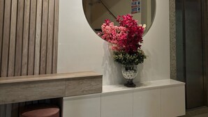 A reception area with a wooden panel wall, a round mirror, and a vase with flowers. - Augusto Palace Hotel (Maraba)