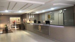 A reception area with a modern design, featuring a reception desk, a clock, and a wall-mounted information board. - Augusto Palace Hotel (Maraba)