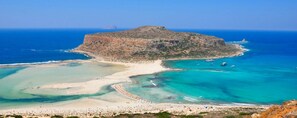 A coastal landscape with a prominent rocky island, clear blue waters, and a sandy beach area.