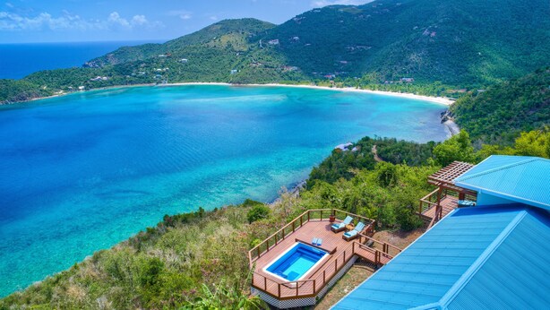 Un resort con piscina en una terraza con vistas al mar turquesa y una playa.
