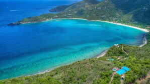 Vista aérea de una zona costera con aguas turquesas cristalinas, una playa de arena y un pequeño edificio con techo azul.