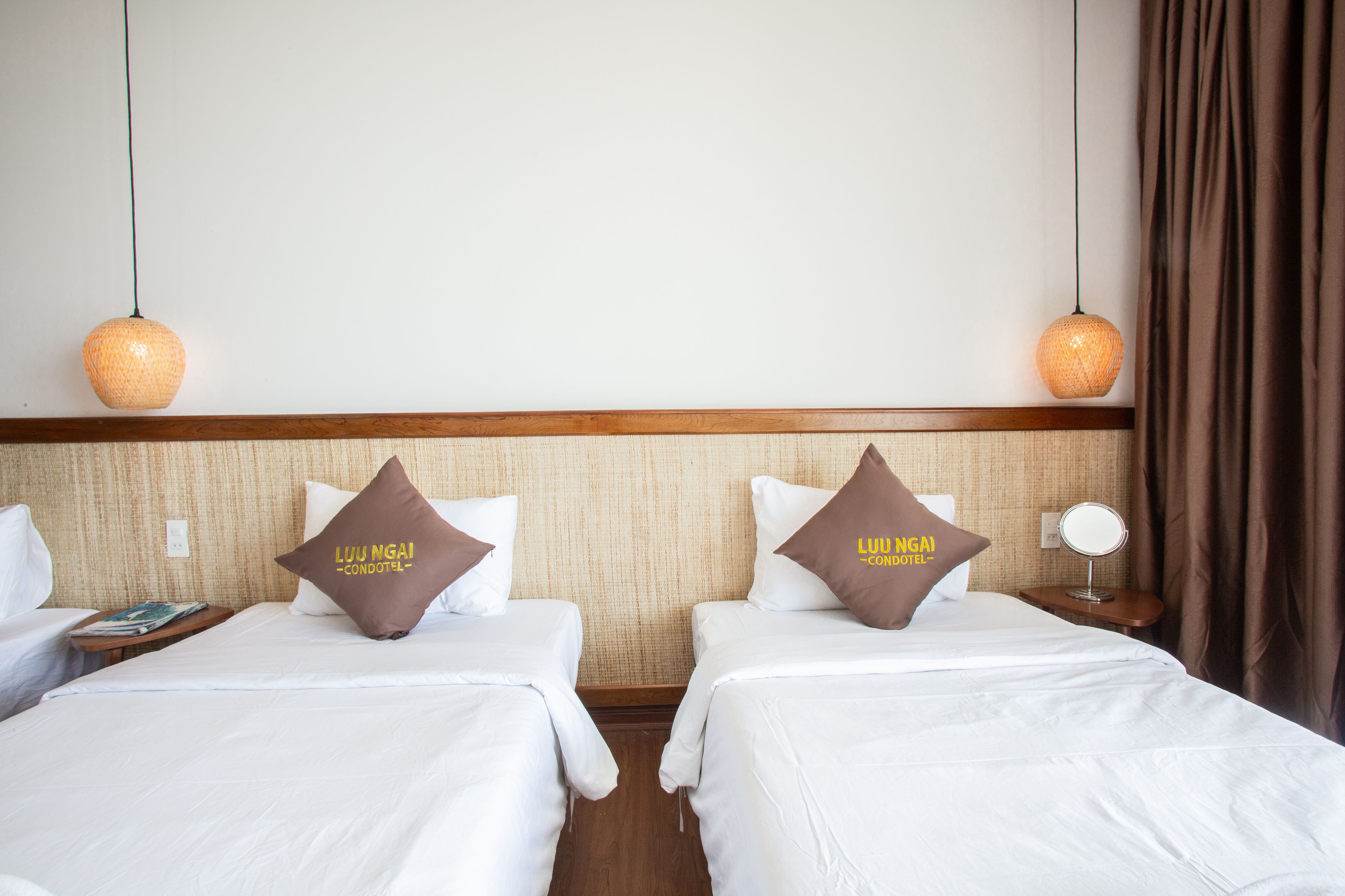 A hotel room with two beds, each with a pillow labeled "Luu Ngan Condotel".