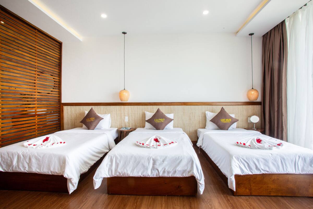 A hotel room with three single beds, each with a wooden headboard, white bedding, and decorative pillows.