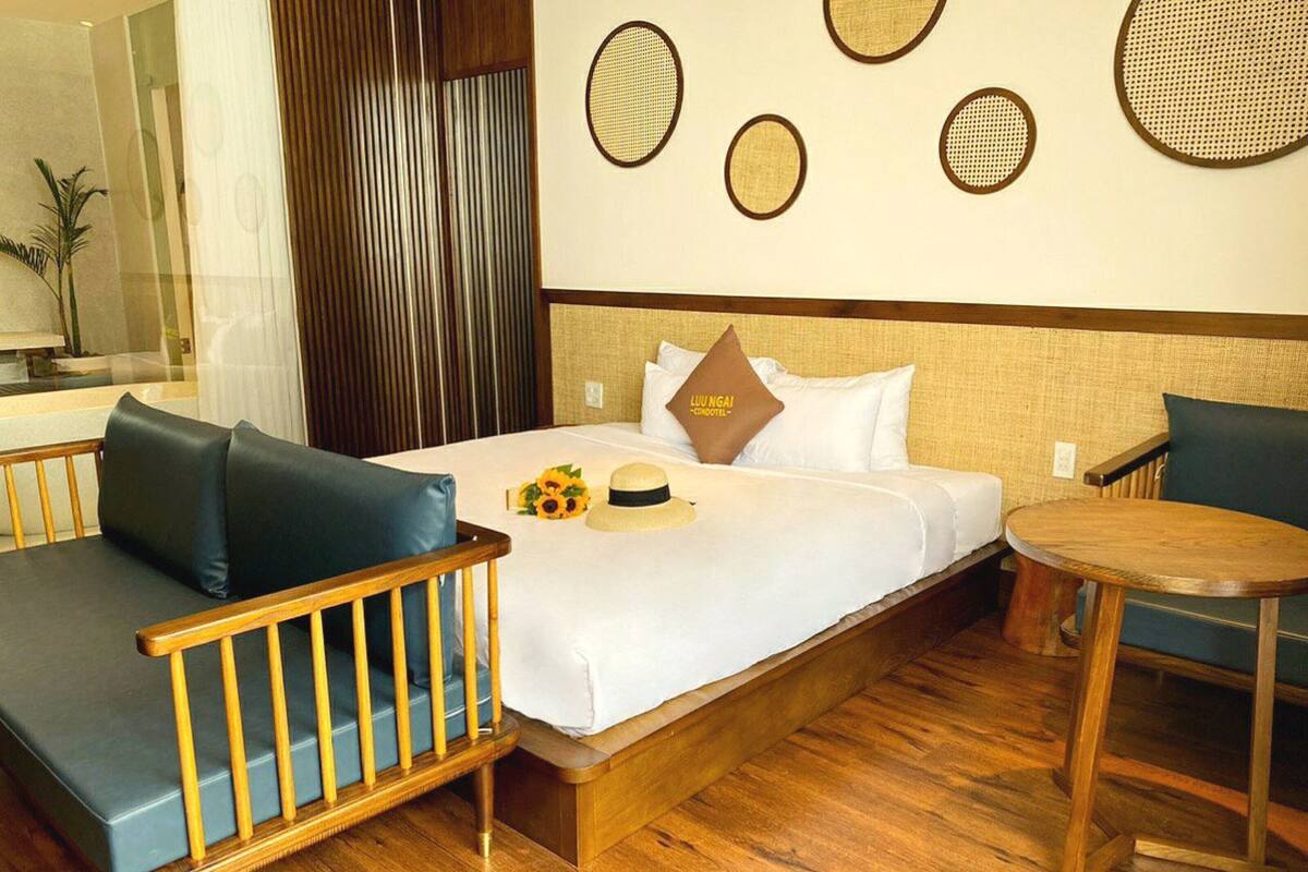 A hotel room with a bed, a wooden bench, a round table, and a wall with circular patterns.