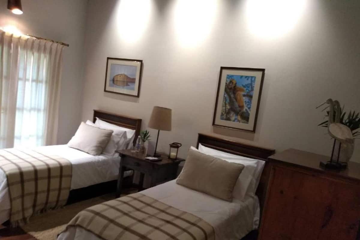 A hotel room with two beds, a nightstand with a lamp, and two framed pictures on the wall.