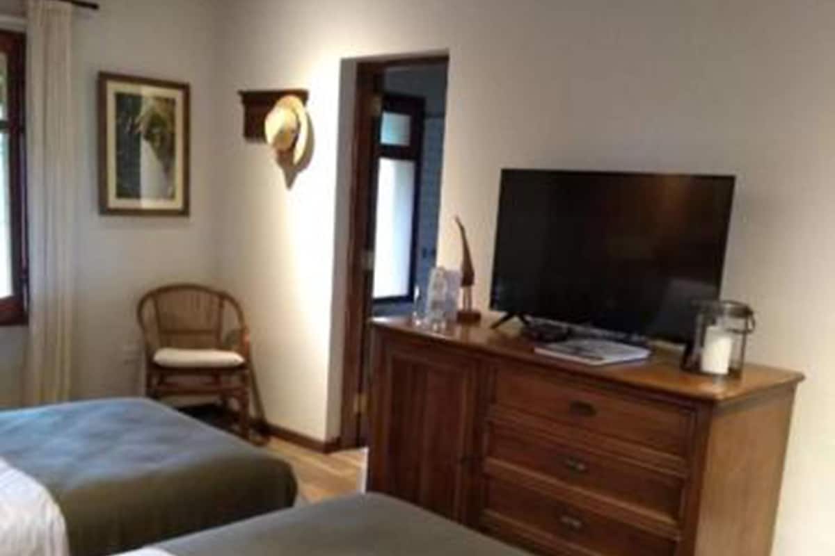 A hotel room with two beds, a wooden dresser, a television, and a chair.