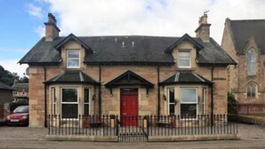 A two-story stone building with a red door, a black roof, and a black metal fence in front. - Gowanfield B&B (Dingwall)