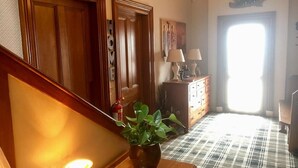 A hallway with wooden doors, a staircase, a potted plant, a table with a lamp, and a checkered floor. - Gowanfield B&B (Dingwall)