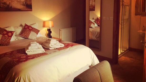 A hotel room with a large bed, a bedside table with a lamp, a mirror, and a shower area. - Gowanfield B&B (Dingwall)